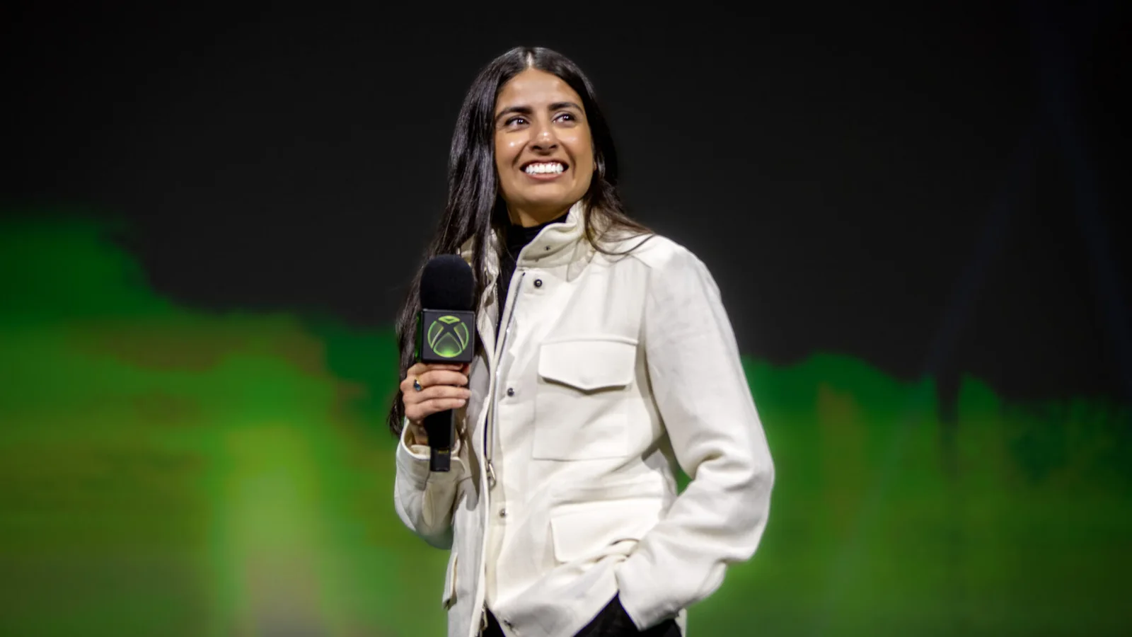 Asha Sharma speaking at the Xbox Games Showcase with a large Xbox logo behind her
