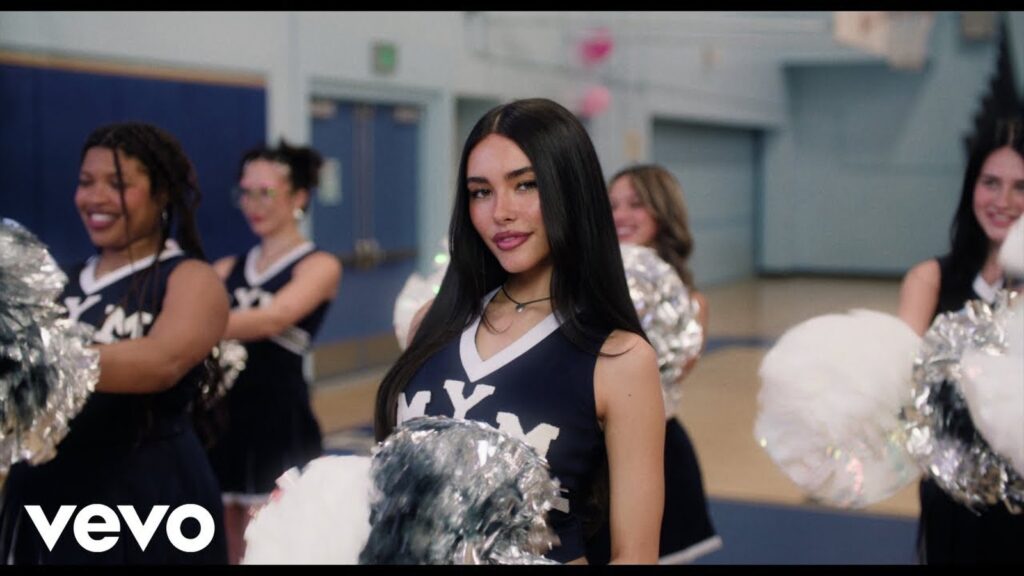 Official still from Madison Beer’s “Make You Mine” music video showing her in a cheerleading uniform inside a school gym