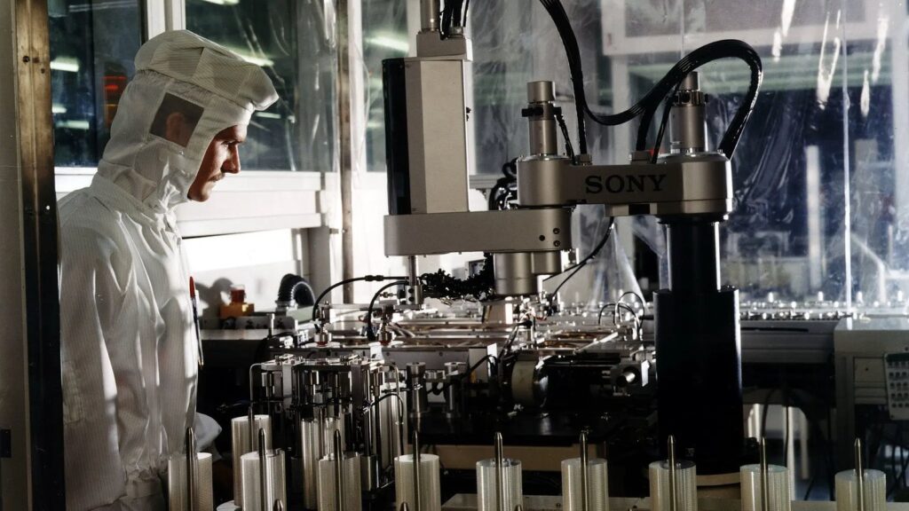 PlayStation Disc Production Decline Figure Corrected by Sony DADC Sony DADC technician working beside Sony-branded automated disc-production machinery inside the manufacturing facility