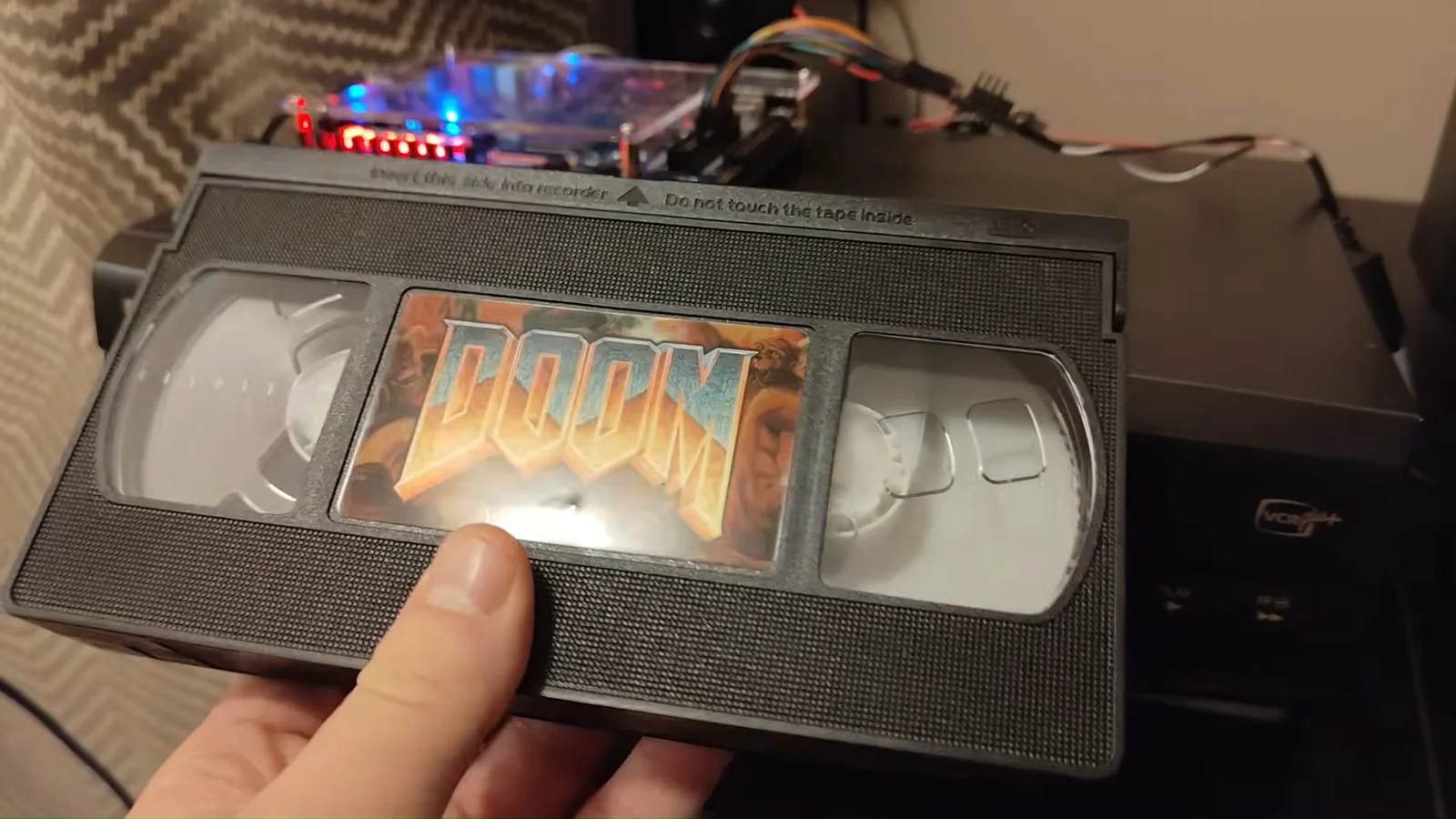 Close-up image of the custom Doom VHS cassette held in front of the project’s VCR and electronics