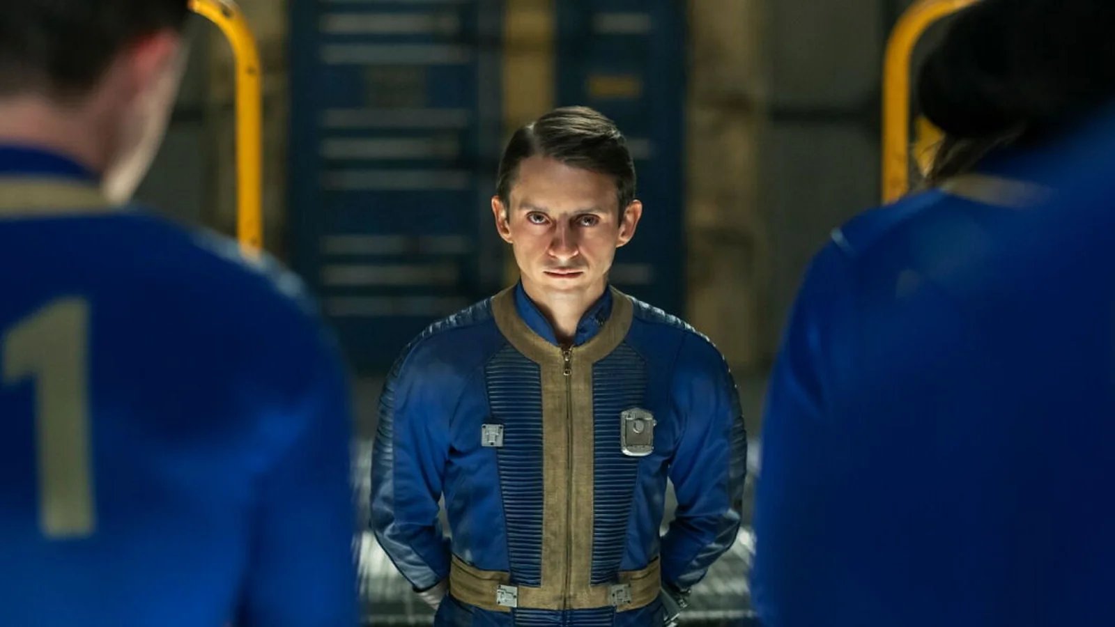 Official Fallout Shelter promotional image showing a man in a blue-and-gold Vault-Tec jumpsuit standing inside a dimly