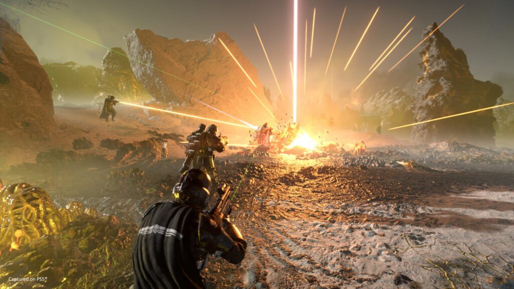 Helldivers 2 Liberty Day 2026 Gives Players a Free Rifle Helldivers squad advancing through an explosive battlefield with rifles, lasers and orbital strikes