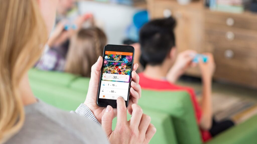 Parent using Nintendo Switch Parental Controls smartphone app while children play Nintendo games in the background