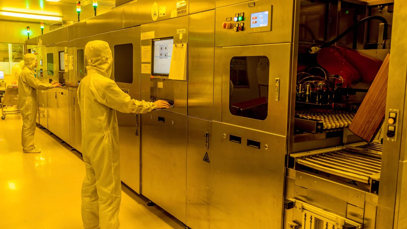 Manufacturing technicians operating PCB processing equipment inside a yellow-lit cleanroom