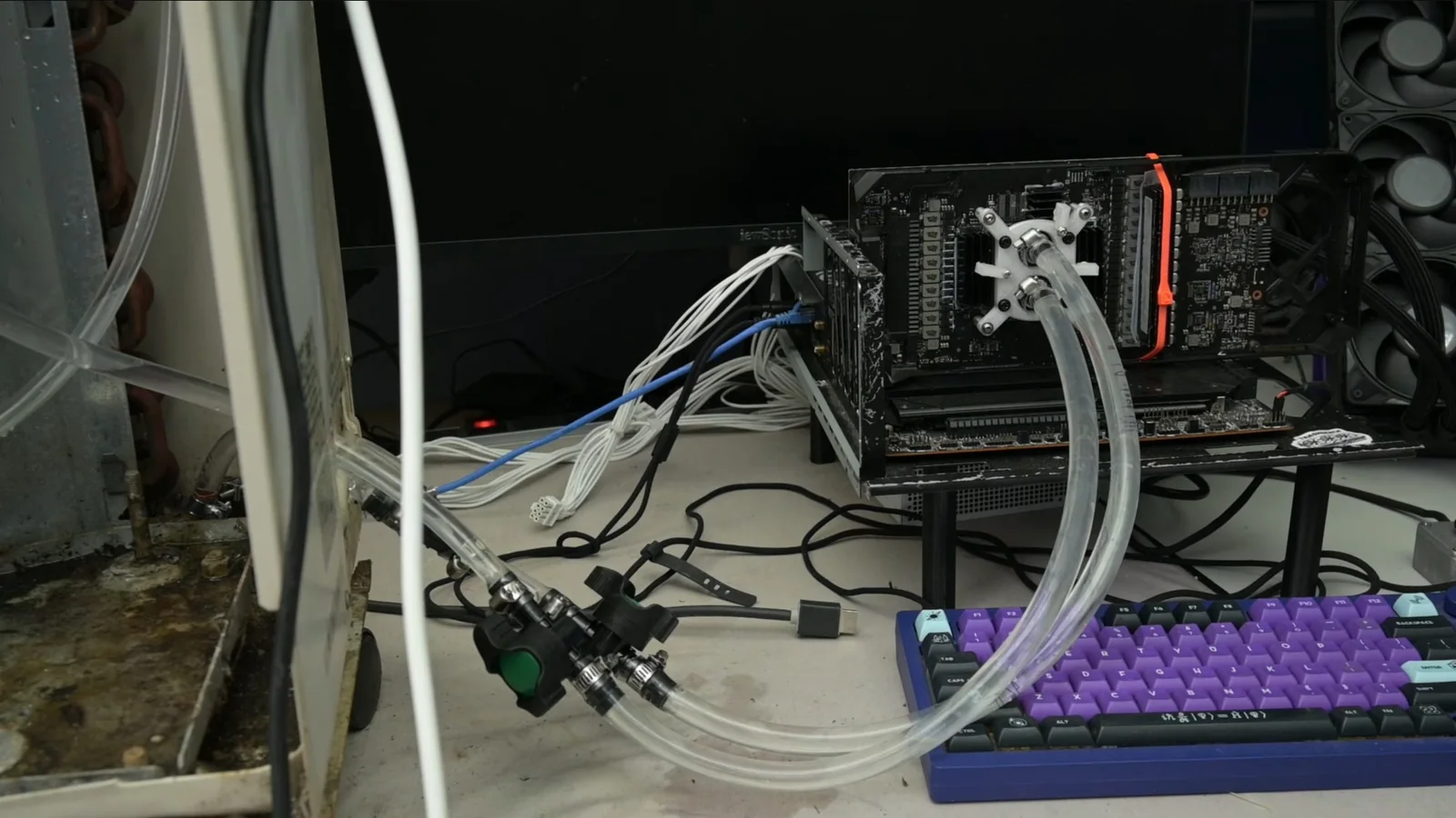 TrashBench's custom GPU liquid-cooling test bench with transparent coolant tubes, exposed graphics card, and external