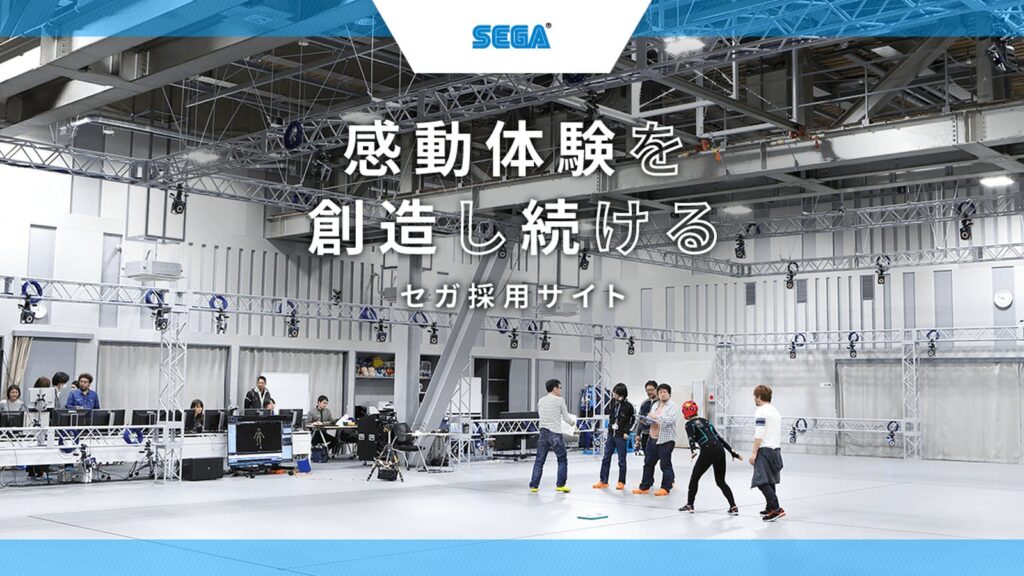 Official SEGA development-division interview image showing two senior developers standing together inside the company’s