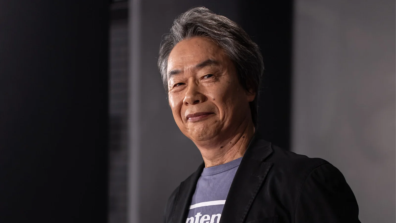 Shigeru Miyamoto wearing a dark blazer and Nintendo T-shirt, photographed against a dark background